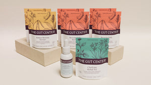 Renew Core set: Radiant Morning and two Reviving Daily Kitchari pouches on a plaster riser, with Clarifying Herbal Tea and a Lightening Hydration Drops bottle.